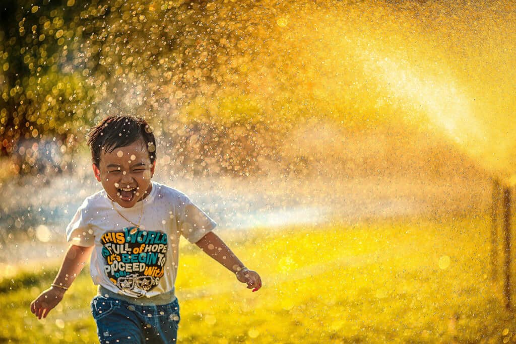 Happy boy playing in sprinklers in the glowing sun