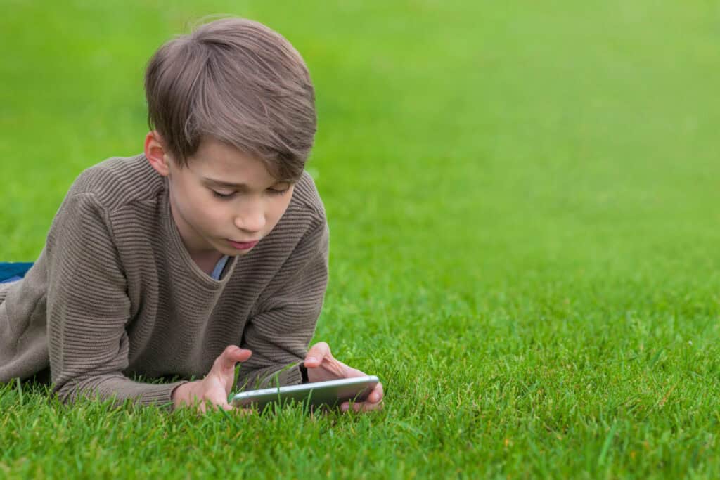 Boy lying in a grass field playing on his iPhone 