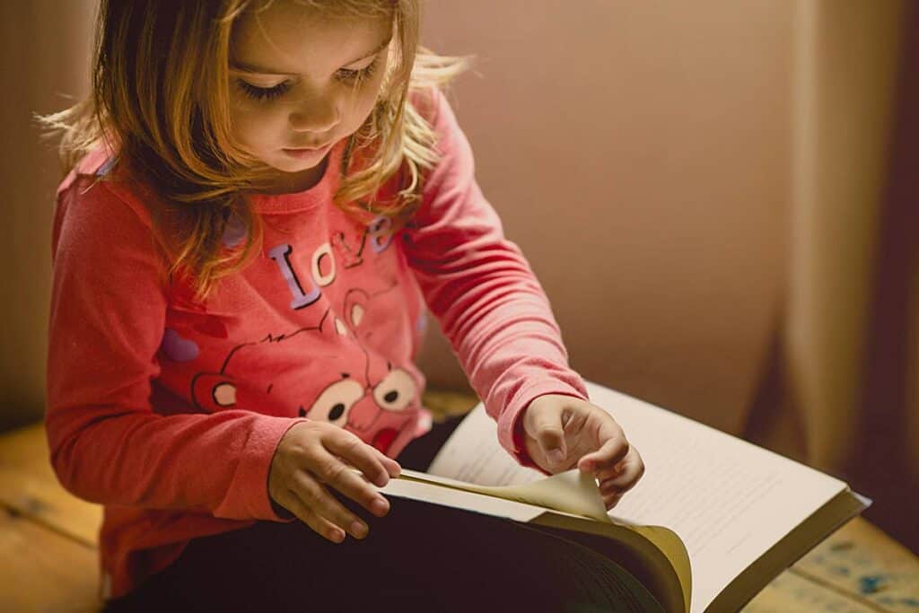Young blond girl turning the page of a book