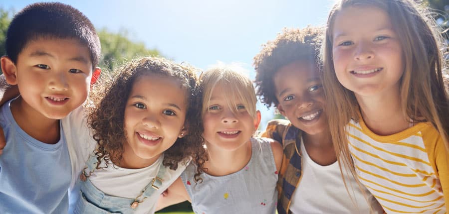 Five mixed race and gender elementary school children smiling with sun shine in the background