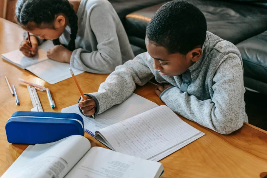 Boy and girl writing in notebooks on a table in front of a couch. 