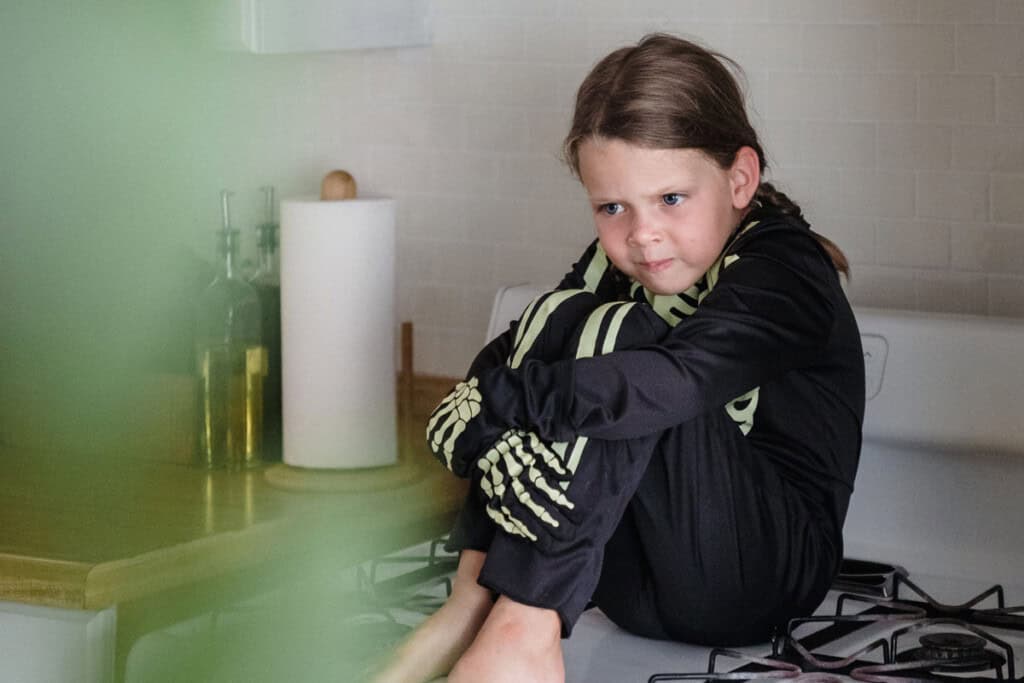 Girl in skeleton costume sitting on stove holding self